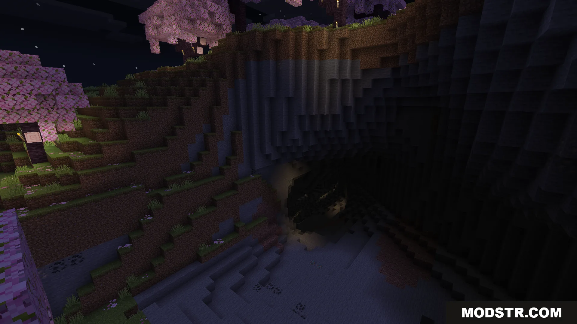 A dark cave entrance nestled beneath a cherry blossom cliff at night