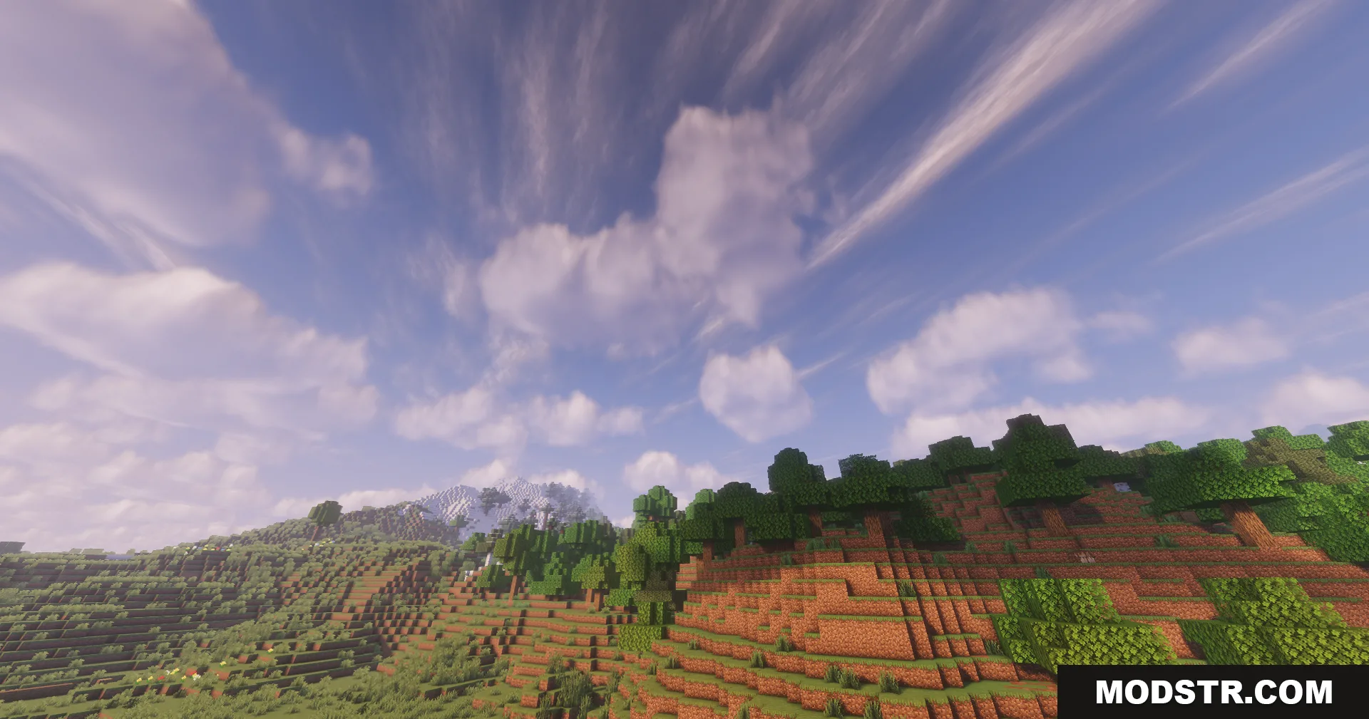 Lush green forest and mountains under a vibrant sky with wispy clouds