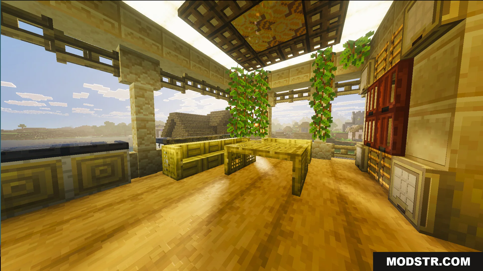 Sunlit balcony area with bamboo furniture and hanging vines overlooking a nearby village