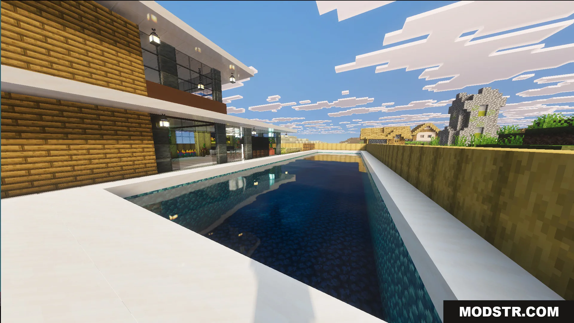 A long swimming pool sits next to the modern house near a village